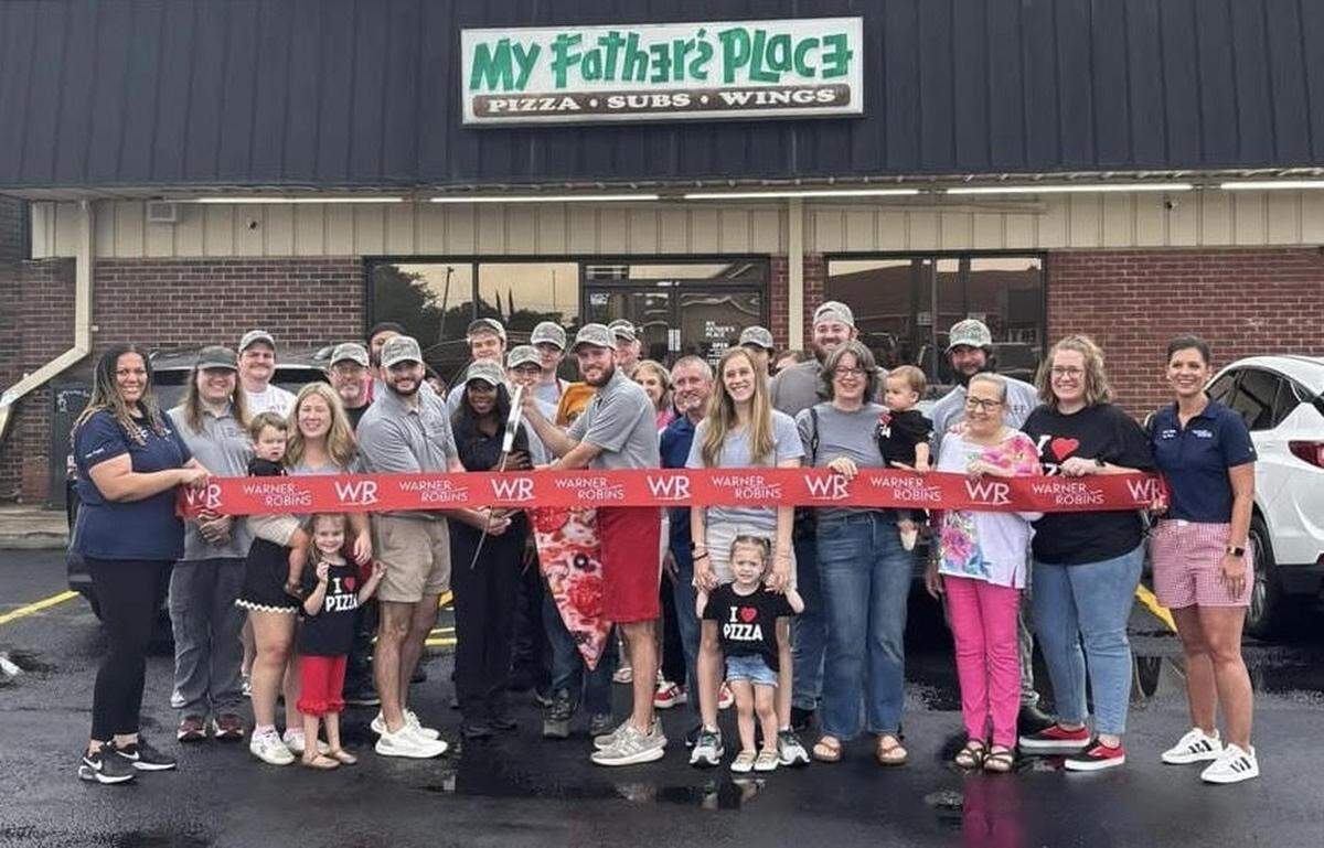 The ribbon cutting for the grand reopening of My Father’s Place in Warner Robins with Warner Robins Mayor LaRhonda Patrick, behind the giant scissors and between co-owners and brothers Jonathan Kline and Jacob Kline and their families, on Aug. 23, 2025. The photo has been cropped.