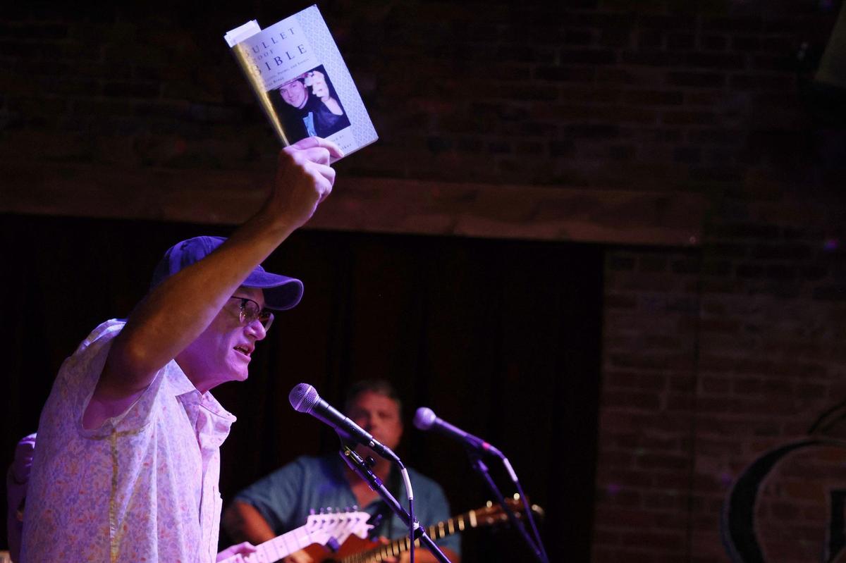 Kirby Griffin holds up a copy of “Bulletproof Bible” during The Buckleys’ set at Bragg Jam on Saturday, July 27, 2024, at Grant’s Lounge in Macon, Georgia. “Bulletproof Bible” is a book of poems and lyrics written by Brax Bragg and compiled after his death in 1999.