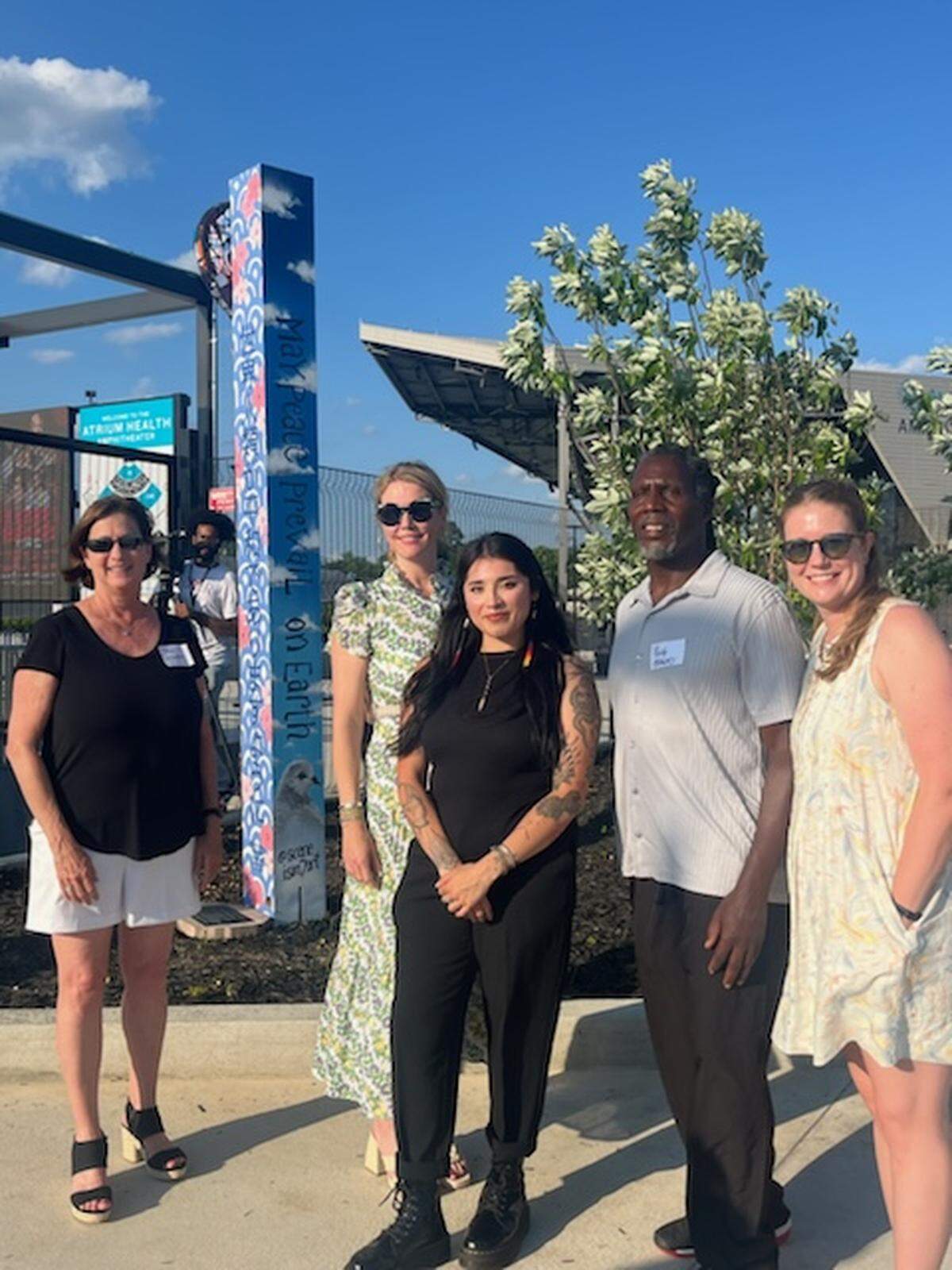 Macon artists stand next to a new Peace Pole at the Atrium Health Amphitheater; each artist painted one side of the pole. The pole was dedicated by the Macon Rotary Club.