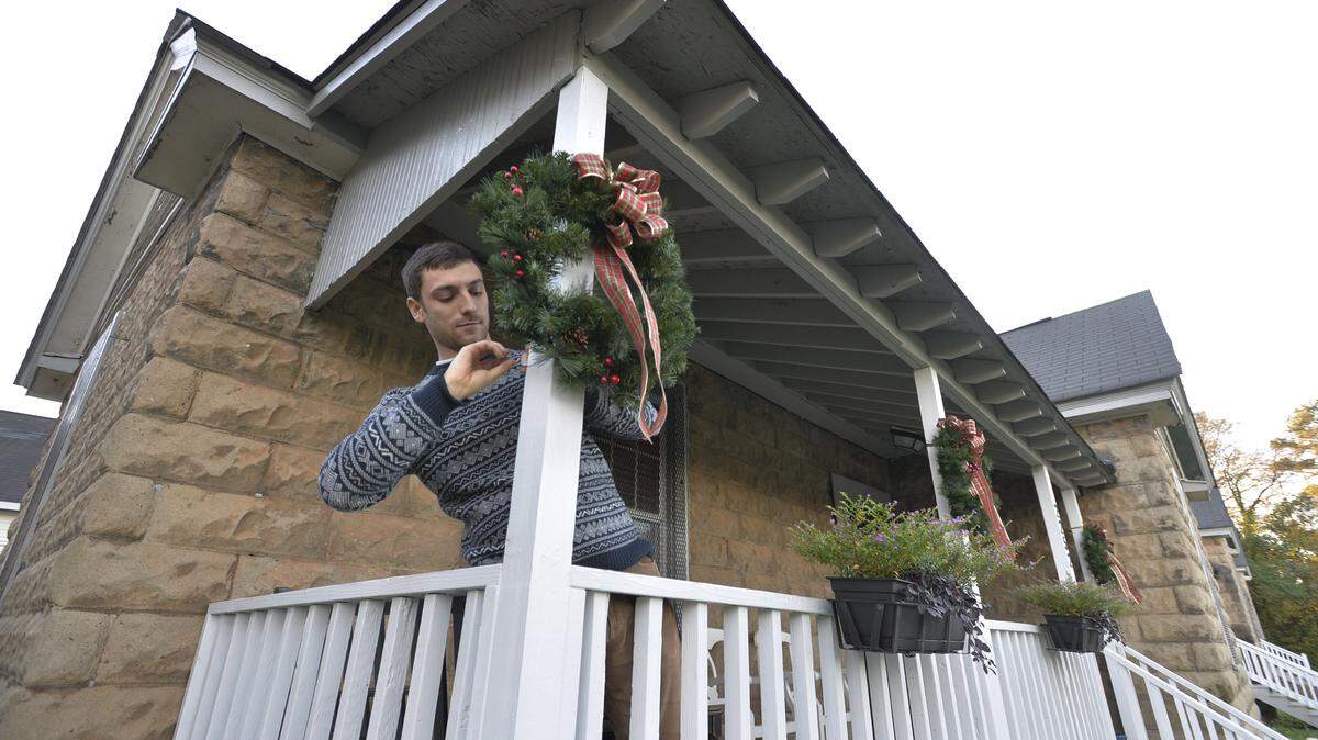 Andrew Berndt puts a Christmas wreath on the porch of his Clayton Street cottage where he and his wife Shari will host a portion of the Vineville Christmas Tour of Homes.