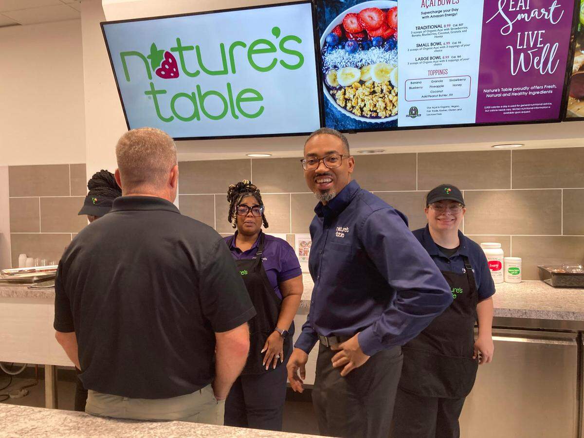 Terrell Robertson, Nature’s Table franchise, looks up from a huddle with employees and a Nature’s Table corporate representative.