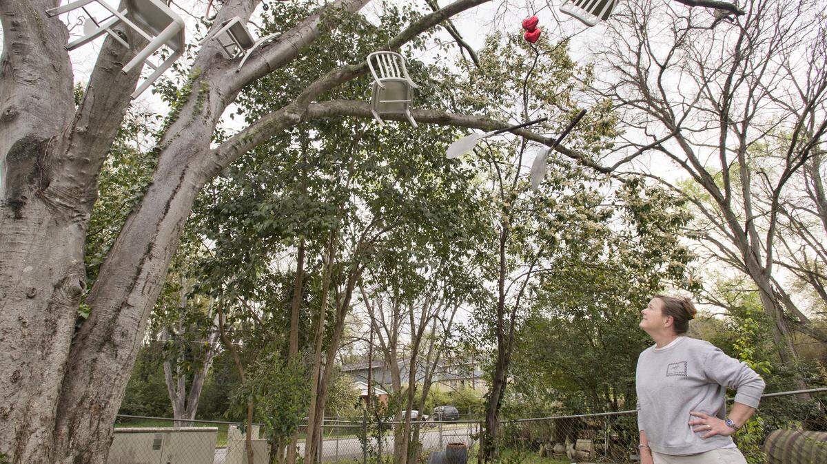 Ingleside Village Pizza owner Tina Dickson stands under a hackberry tree behind the restaurant Friday. Dickson decided one day to rent a bucket truck and hang old chairs, pizza peels and an employee's bike in the tree.