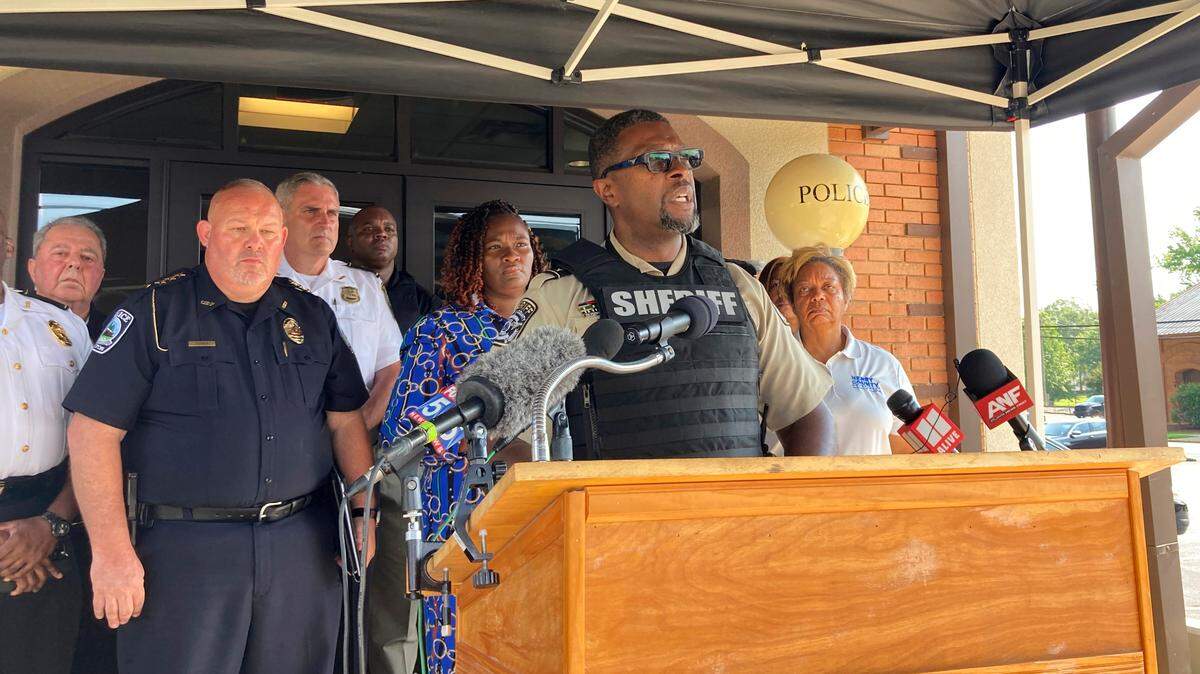 Henry County Sheriff Reginald Scandrett speaks in Hampton while flanked by other police and local officials. Scandrett announced that officers shot and killed Andre Longmore Sunday, a day after officials say Longmore killed four Hampton residents.