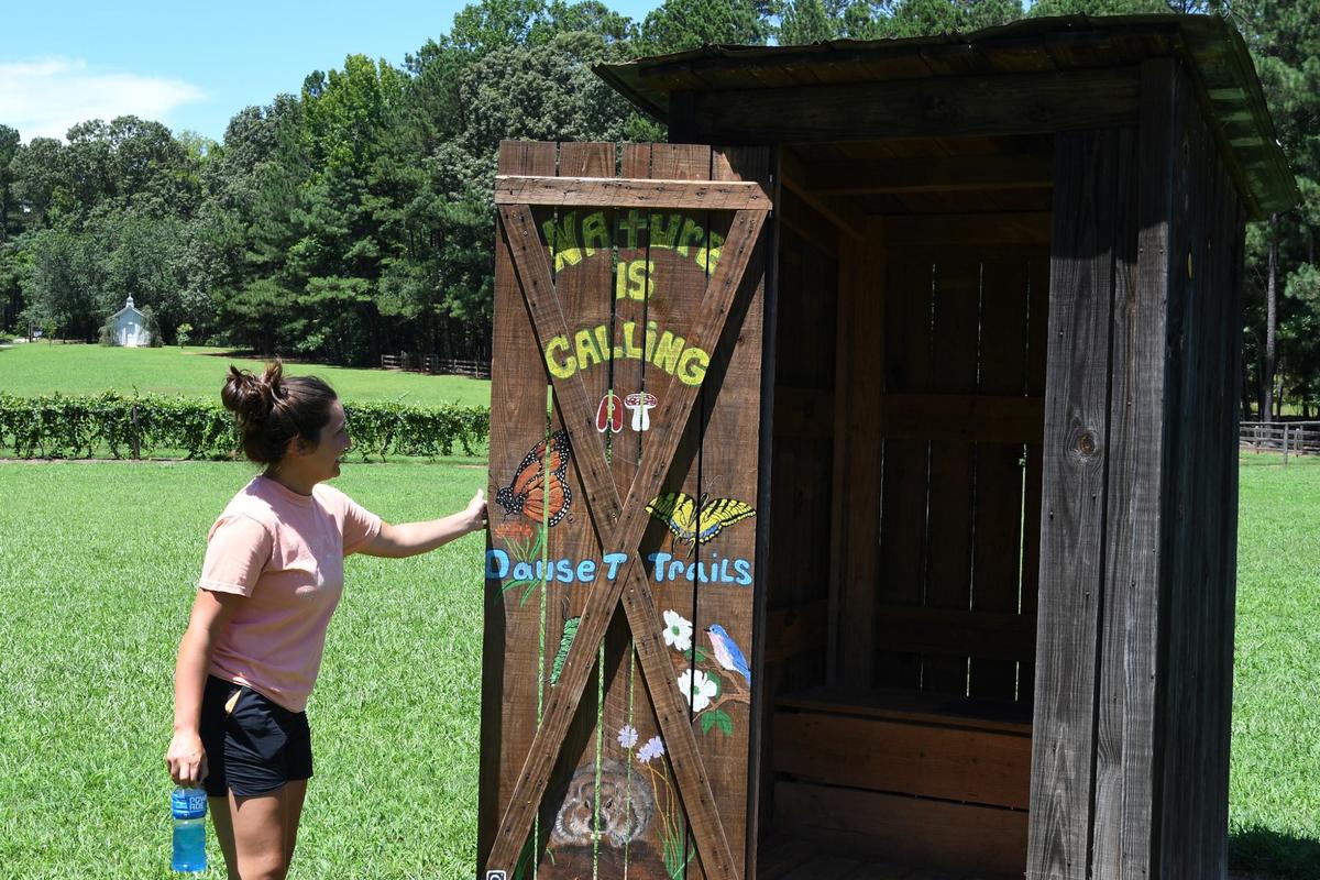 Dauset Trails Nature Center head animal caretaker Madelyn Brown opens a model outhouse painted by the center’s maintenance team at Dauset Trails Nature Center on Thursday, July 11, 2024, in Jackson, Georgia. Dauset Trails Nature Center is a private, non-profit environment education organization with almost 2,000 acres of grounds, Georgia animals on exhibit and 30 miles of trails.