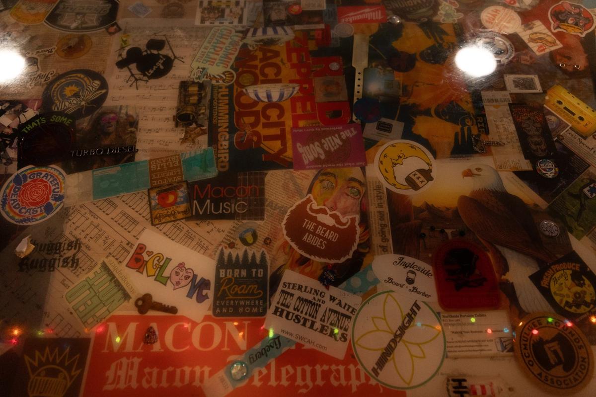 A countertop filled with local stickers, decals and pins sits in the center of T & Jay’s Bar on Tuesday, May 14, 2024, in Macon, Georgia. Owner Terrell Landry said that he and his friends all contributed the items inside the tabletop.