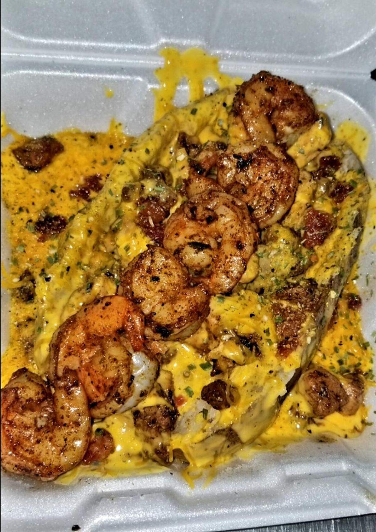 A loaded potato draped with cheddar cheese drip, sprinkled tater dust and chives and topped with filet steak, shrimp and bacon from Potato Po-Ta-Toe in Bonaire.