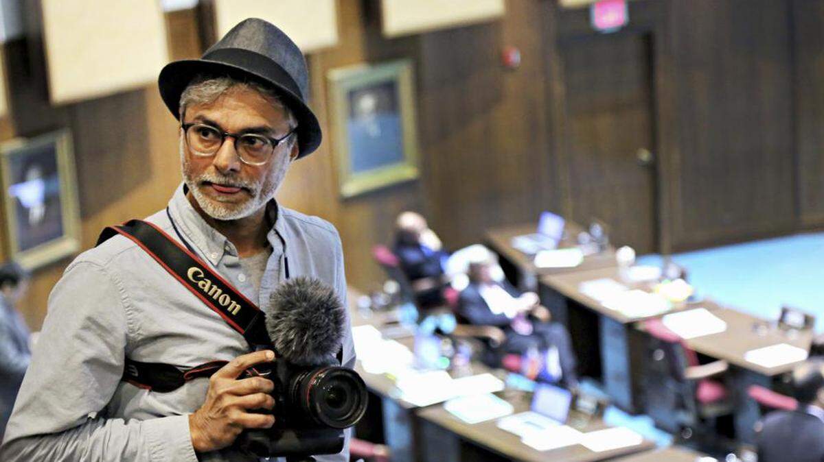 In this 2016 file photo Arizona Republic photographer Nick Oza interviews Capitol Media Services reporter Howie Fischer. Pulitzer Prize-winning Arizona photojournalist Oza, who documented the lives of disaster victims and immigrants, has died at age 57, on Sept. 27 after being hospitalized with injuries from a traffic accident.
