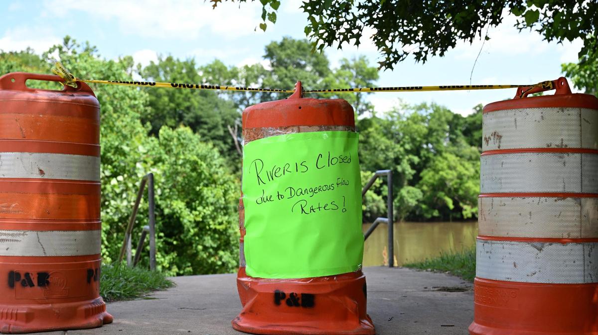 A poster hangs from traffic cones closing off a swimming area of Amerson River Park on Friday, May 23, 2025, in Macon, Georgia. Access to the Ocmulgee River is closed until further notice due to dangerous river speeds.