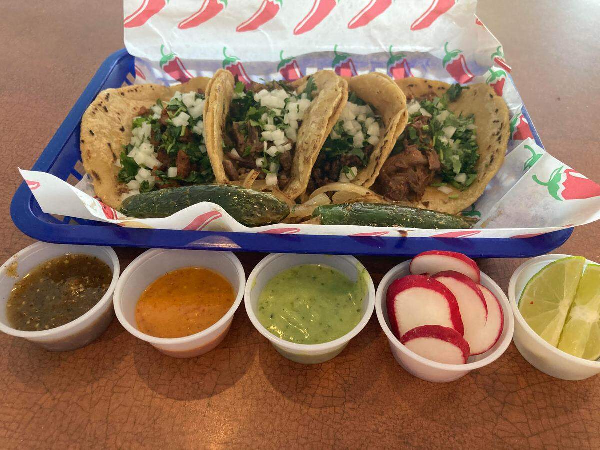 A serving of tacos from Taqueria Don Sammy. From left to right, al pastor (barbecue pork), asada (grilled steak), chorizo (sausage) and barbacoa (shredded beef), with jalapenos and grilled onions along with tomatillo, chili arbol and avocado sauces, sliced radishes and limes.