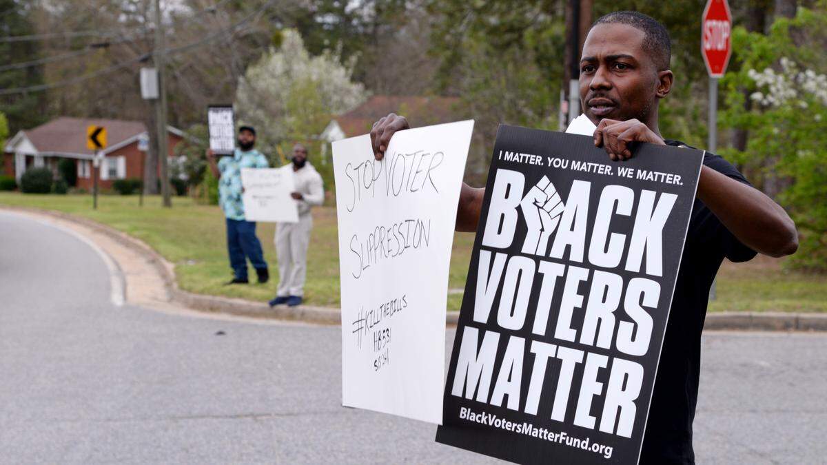 L. J. Malone holds signs at the entrance of the Coca-Cola Bottling Co. on Rocky Creek Road as part of a Black Voters Matter campaign to hold large corporations accountable. Coca-Cola and many other companies pledged to support racial equity during the summer of protests in 2020 following the deaths of George Floyd, Breonna Taylor and Ahmaud Arbery. Black Voters Matter is trying to get those same companies to help them fight voter suppression in Georgia.