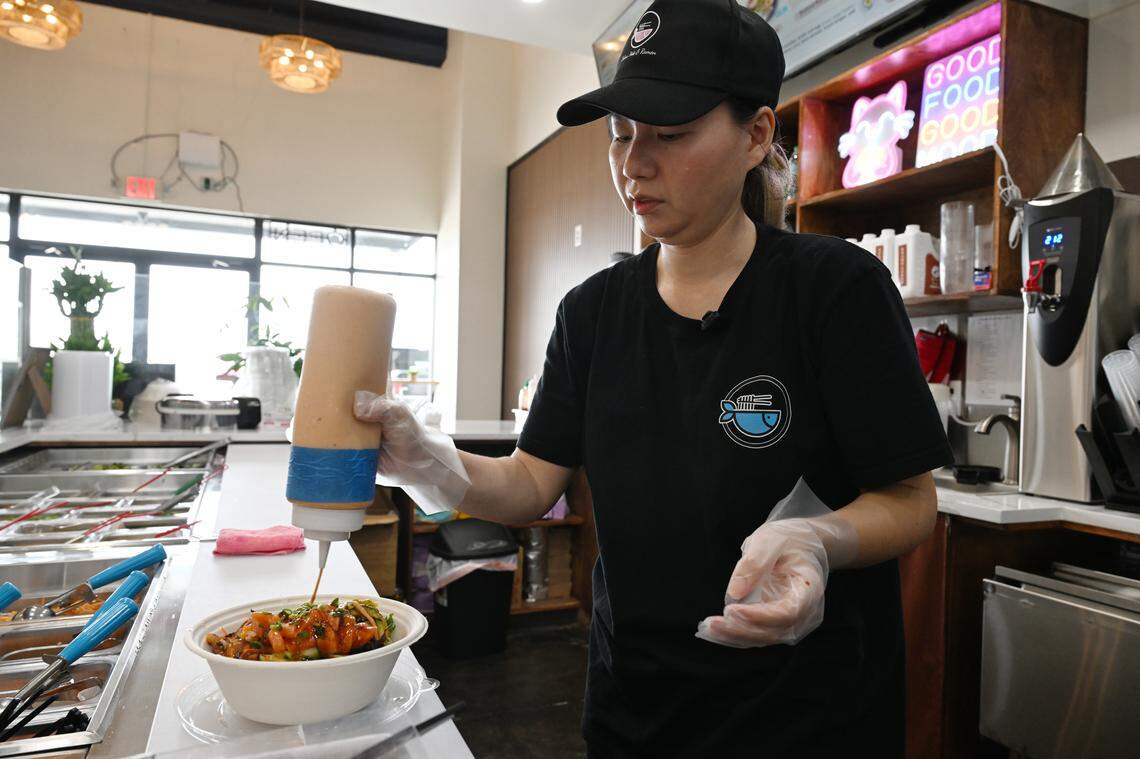 Robins Poke & Ramen co-owner Yazhen “Jenny” Dong adds house poke sauce to a take-out poke bowl order.