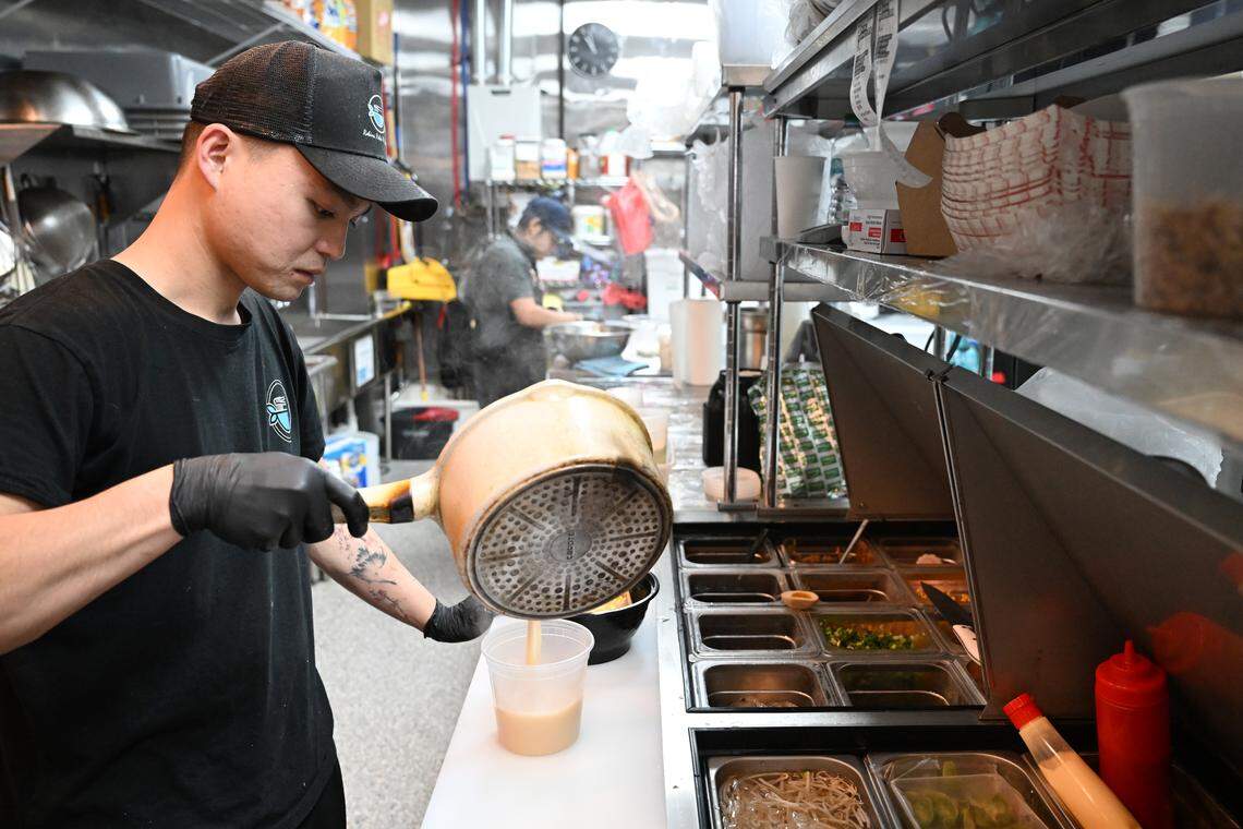 Robins Poke & Ramen co-owner Bin Dong pours ramen broth into a take-out container.