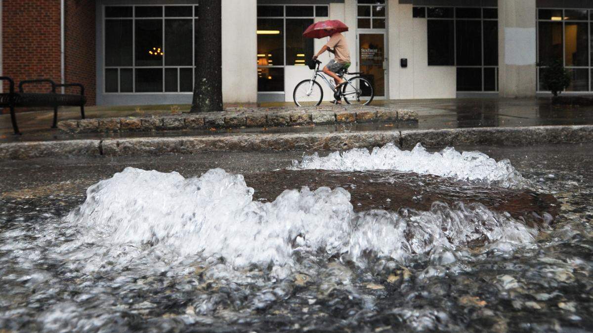 A bicyclist holds an umbrella on the Cherry Street sidewalk as water gushes from a manhole in this file photo from 2013. An afternoon storm had dumped more rain than the stormwater system could handle.