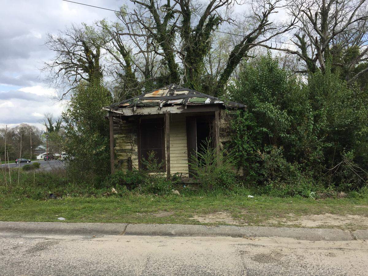 The door stands wide open on a dilapidated vacant home in Pleasant Hill, surrounded by unkempt, bulldozed lots on either side.