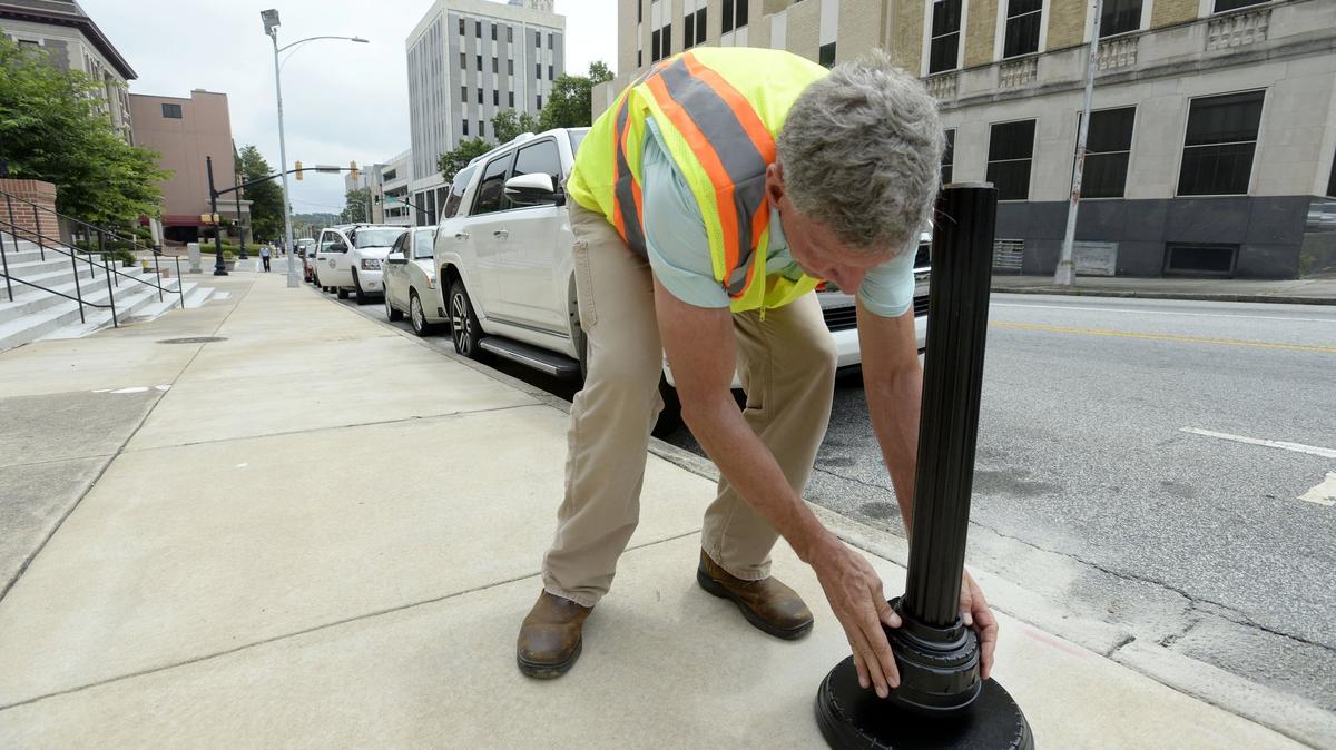 In June, Bill Causey slides black sleeves over the newly installed base of a parking meter in front of the Macon City Auditorium where crews were busy marking and installing the hardware.