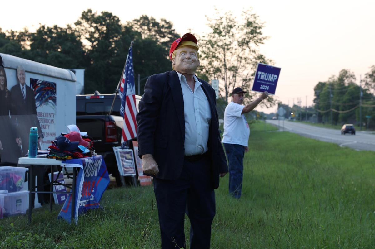 Bibb County Republican Party chairman David Sumrall stands in a Donald Trump mask on the side of Eisenhower Parkway on Monday, July 15, 2024, in Lizella, Georgia. A half dozen supporters, including members of the Bibb County Republican Party, gathered to show their support for former president Trump two days after an attempted assassination attempt on him in Pennsylvania.