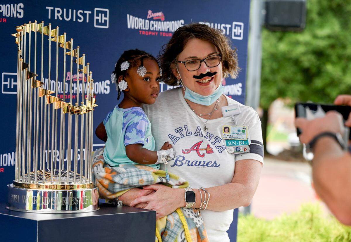 Cyndee Jones, RN, holds patient Journey Brown, 2, while getting their photo taken with the Atlanta Braves 2021 World Series Trophy outside of Beverly Knight Olson Children’s Hospital Tuesday morning. Jones is a huge Braves fan and stopped at a local store to pick up a removable mustache to resemble pitcher Spencer Strider.