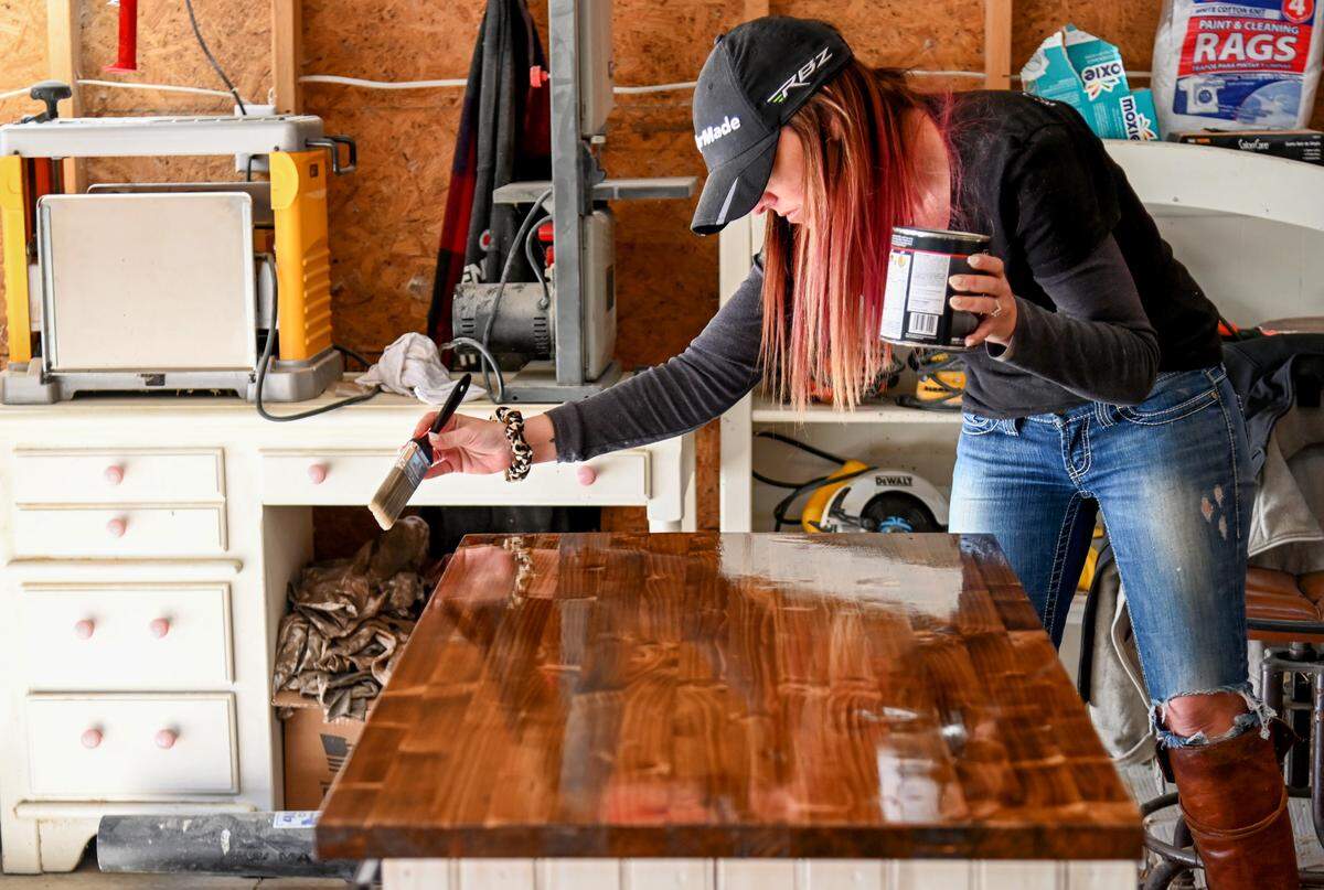 Heather Peebles, owner of Penelope’s Farmhouse Furniture, puts a coat of polyurethane on an entertainment center she’s making for a client in her workshop at her home in Byron.