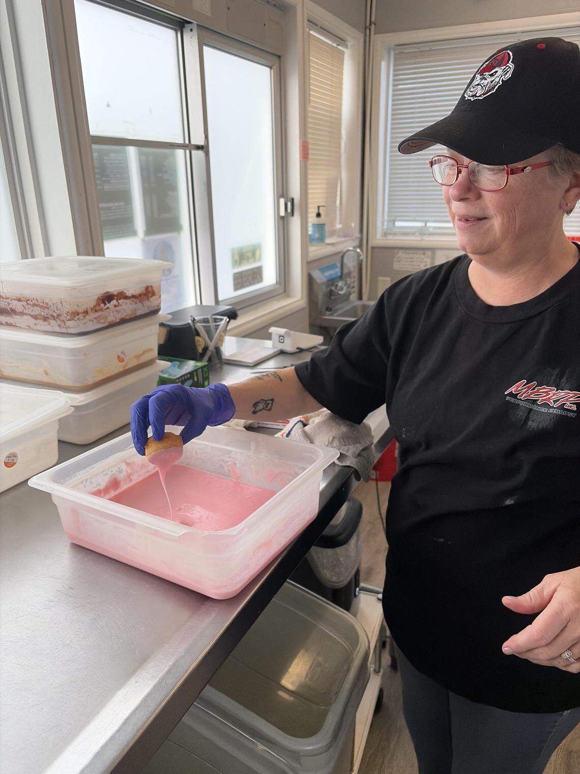 Little Light Coffee Co. doughnut maker Tammy Simmons dips a vanilla cake mini doughnut into strawberry icing.