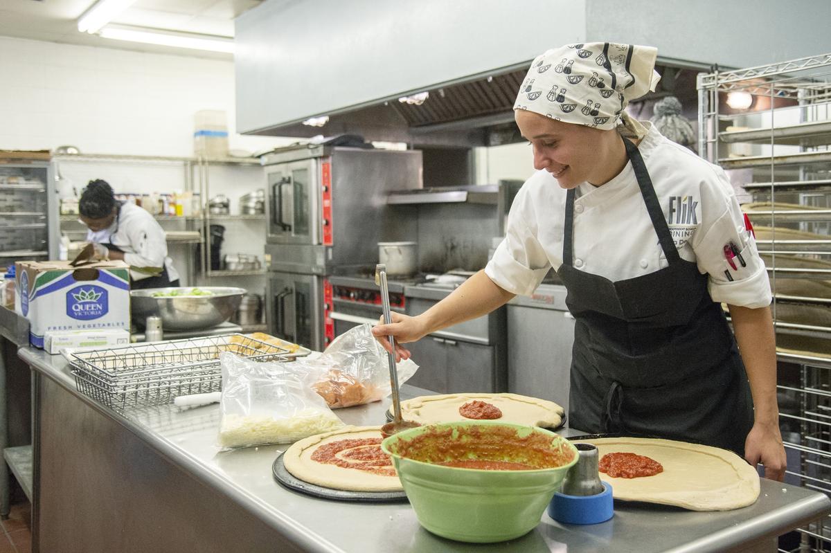 Amelia DeAngio, executive chef for Flik Independent School Dining, spreads sauce on whole wheat pizza dough Wednesday morning in the kitchen at Stratford Academy.