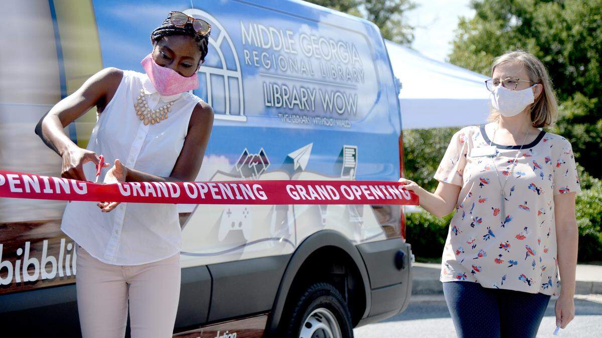 Jennifer Lautzenheiser, right, director of Middle Georgia Regional Library helps hold a ribbon as Tonja Khabir, executive director of Griffith Family Foundation cuts the ribbon for the new “Library Without Walls” outreach vehicle Wednesday at the Mulberry Market at Tattnall Square Park. The library recently received a $20,000 grant from the Griffith Family Foundation to purchase the vehicle.