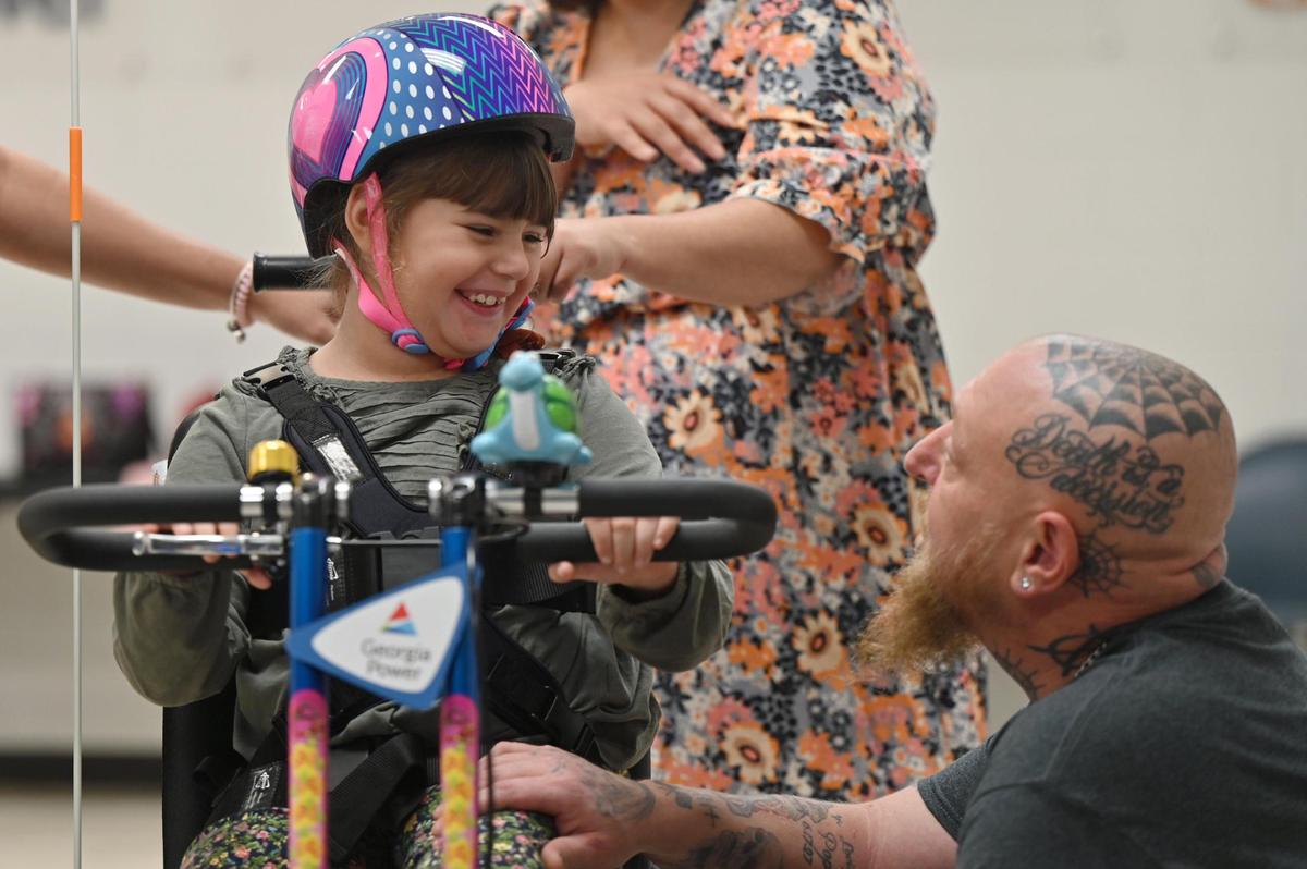 Stella Promesti-Adamek, 7, from Warner Robins, (left) smiles at her dad Richard Adamek after receiving her new adaptive bicycle gifted to her by Georgia Power on Tuesday, Nov. 19, 2024, at the Georgia Power Company in Macon, Georgia. The bicycle was custom designed by Freedom Concepts and usually costs between $4500 and $5000.