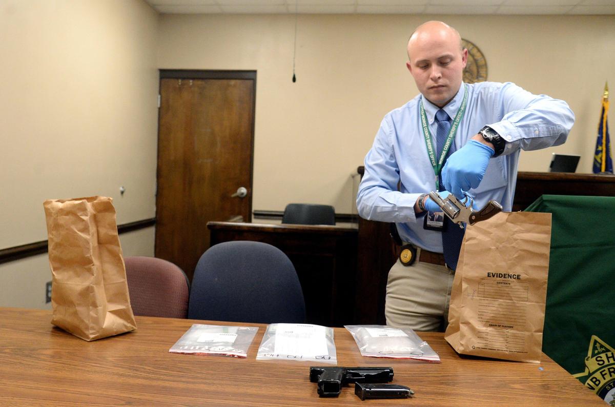 Monroe County investigator Jacob Robins places a hand gun on a table at the Monroe County Sheriff’s Office recovered after capturing two suspects from a high speed chase Tuesday evening.