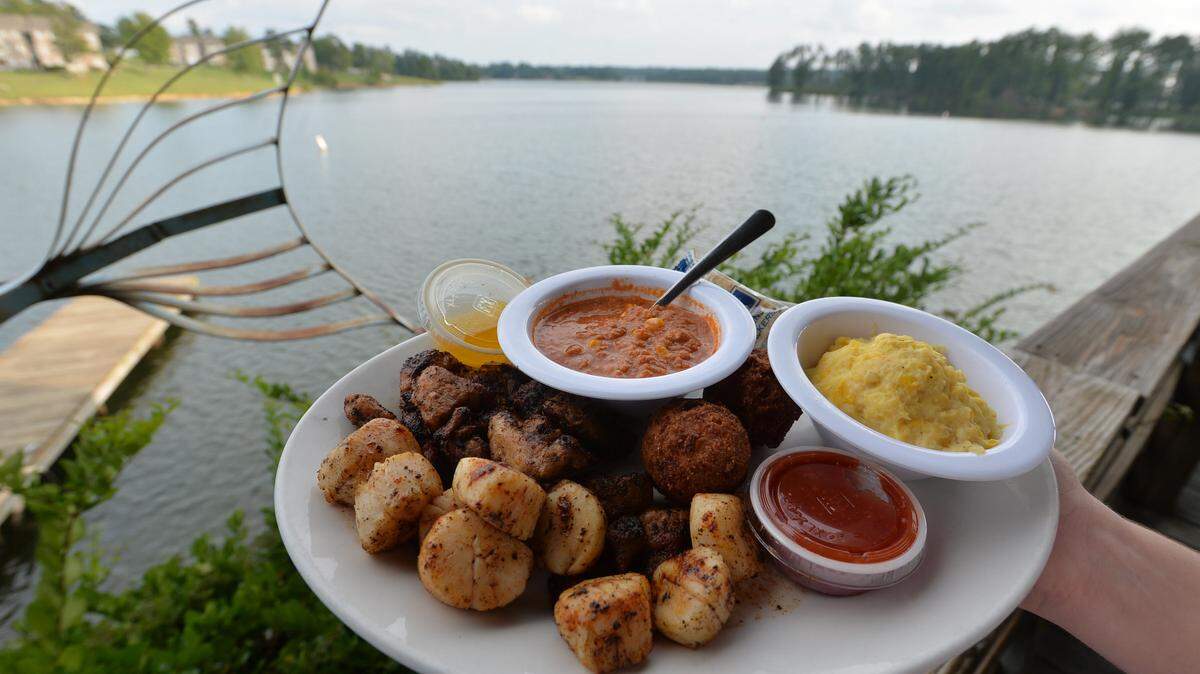 A combination platter of alligator and scallops is served with side items of Brunswick stew and casserole, along with a view of Lake Tobesofkee, at the Fish N’ Pig.