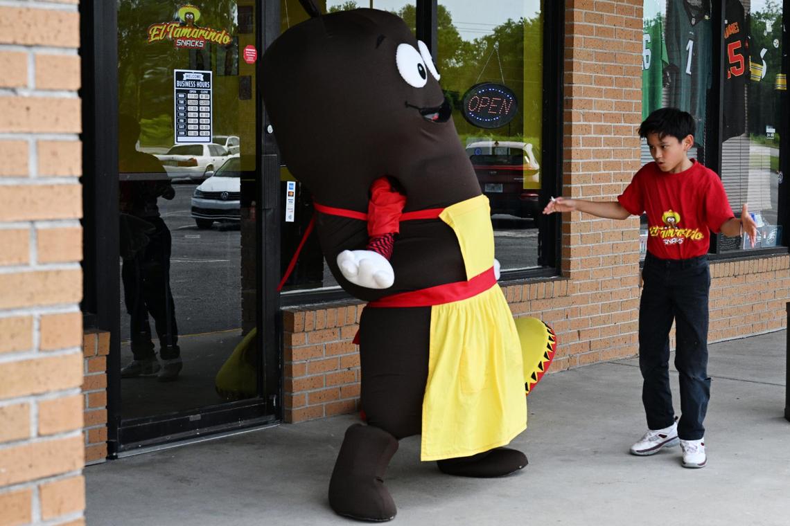 Delsy Reyes (left), sister of part owner Jeniffer Reyes, dresses up in a mascot costume and dances outside of El Tamarindo Snacks with nephew Jayden Reyes on Friday, May 16, 2025, in Macon, Georgia. El Tamarindo Snacks opened in April and offers a variety of Mexican snacks, desserts and beverages.