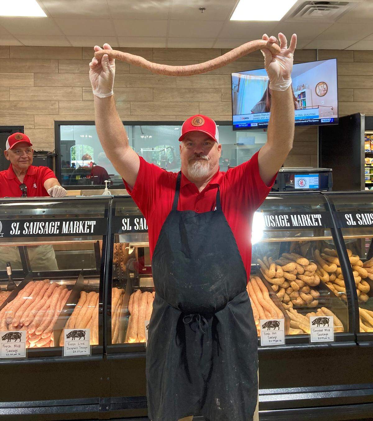 Matt Womack holds up a link of sausage at the newly-opened SL Sausage Company in Macon while co-worker Buddy Roper looks on.