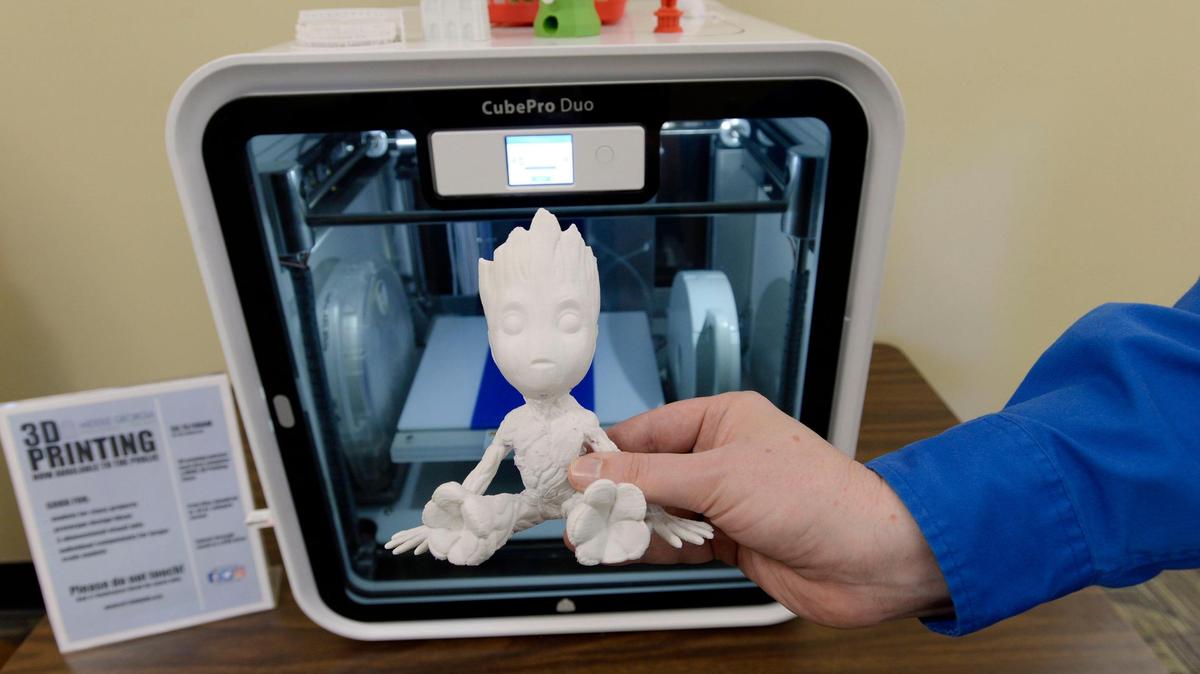 Kevin Bryant holds one of the items printed on the Washington Library’s new three dimensional printer, at rear, which is about the size of a microwave oven. Librarians are holding classes on how the use the device.