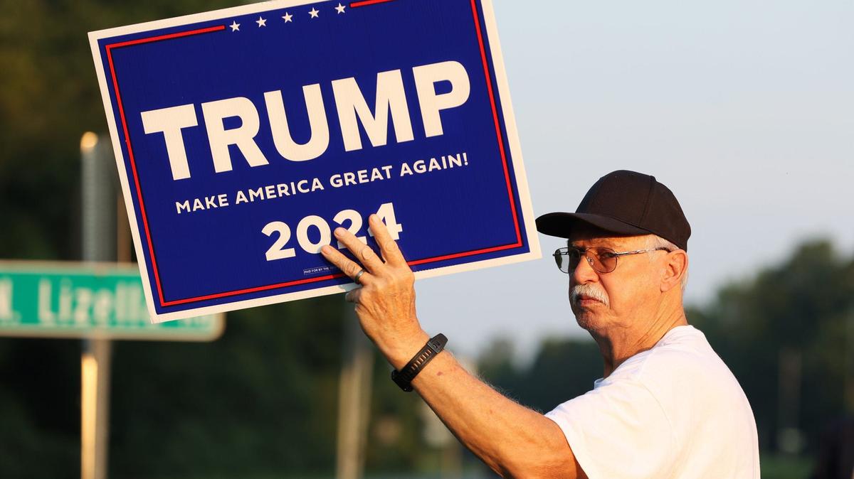Aubrey Clark stands with a Trump 2024 sign on the side of Eisenhower Parkway on Monday, July 15, 2024, in Lizella, Georgia. A half dozen supporters, including members of the Bibb County Republican Party, gathered to show their support for former president Trump two days after an attempted assassination attempt on him in Pennsylvania.