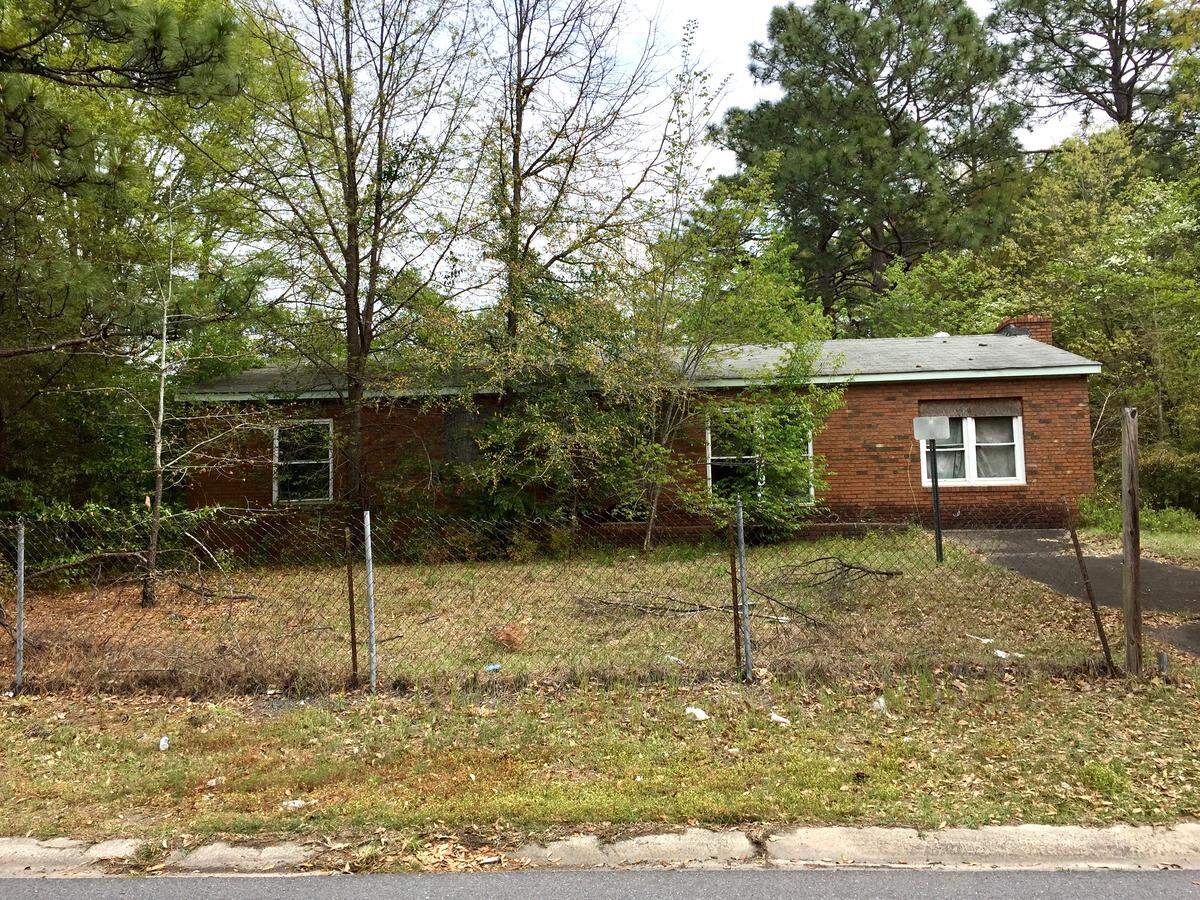 Dead tree limbs and overgrown weeds litter the yard of an empty property across the street from Theresa Hugley’s house on Kings Park Circle.