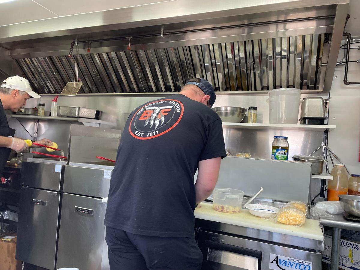 Mark Bell, right, general manager of the Bearfoot Tavern in downtown Macon, and Scott Heck, the gastropub’s kitchen manager, prepare eats in the food truck Wednesday, Feb. 26, 2025, in the Lowe’s Home Improvement parking lot off Watson Boulevard in Warner Robins. The photo was taken through a counter window.