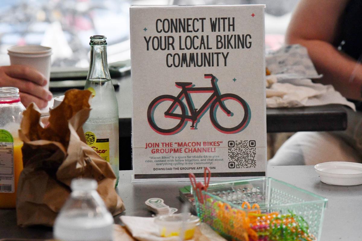 A sign advertising a “Macon Bikes” group chat sits on a table during the Car Free Day meetup on Friday, May 24, 2024, at Macon Bagels in Macon, Georgia. Macon Car Free Day is an annual event sponsored by Bike Walk Macon that encourages alternative transportation throughout the city.