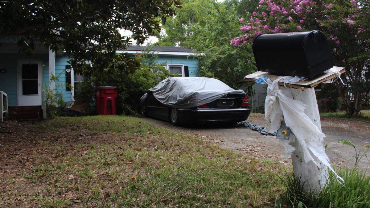Grass was unkempt and a car was half-covered with a tarp outside a house on Kings Park Circle in Macon, Ga. on Wednesday, Aug. 14, 2024. A man who lived here was found dead in his home Aug. 8 after rotting for weeks, according to Bibb County Coroner Leon Jones.