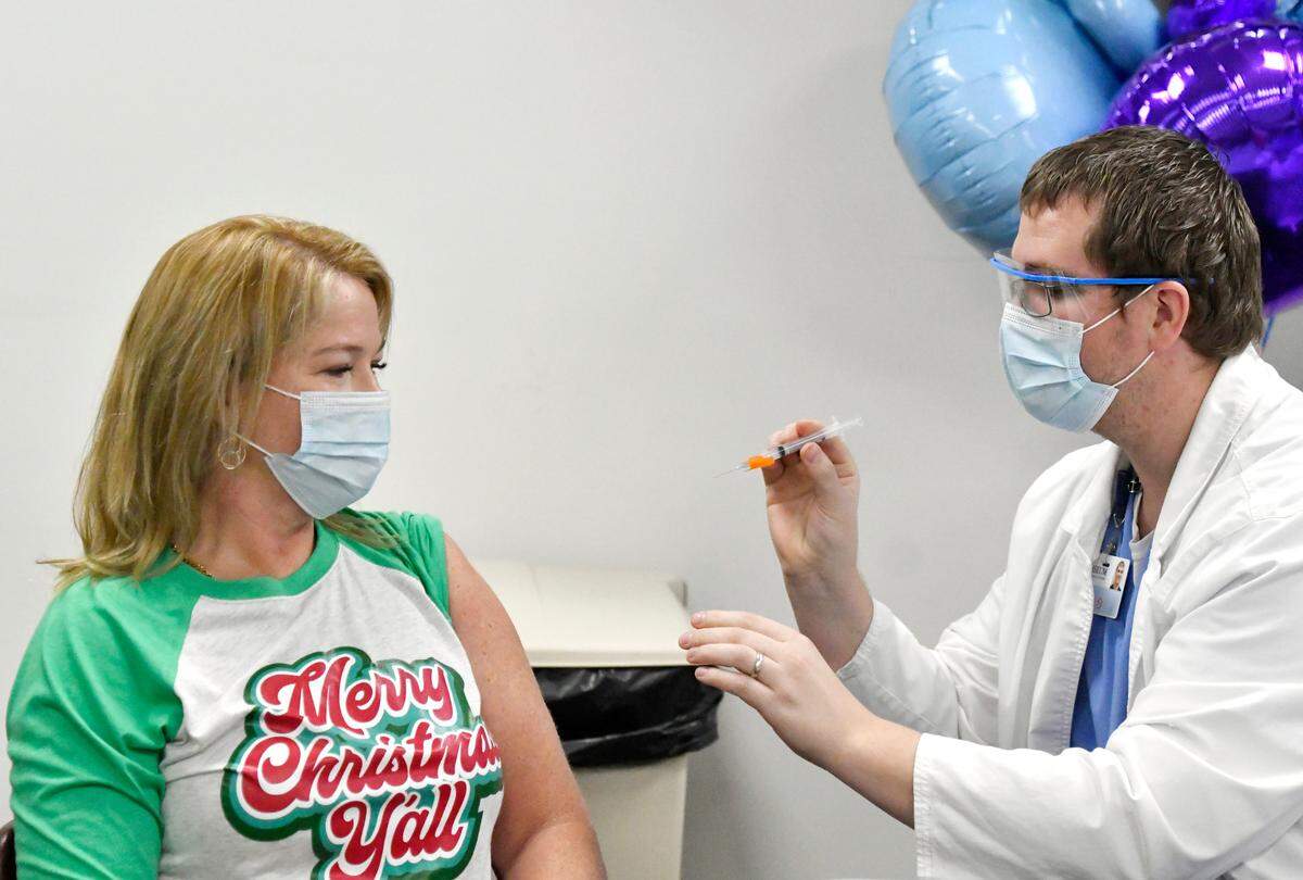 Laney Hogan, a registered nurse in the ICU at Coliseum Medical Centers, receives the Moderna COVID-19 vaccine Thursday from fellow RN Ben Kerscher.