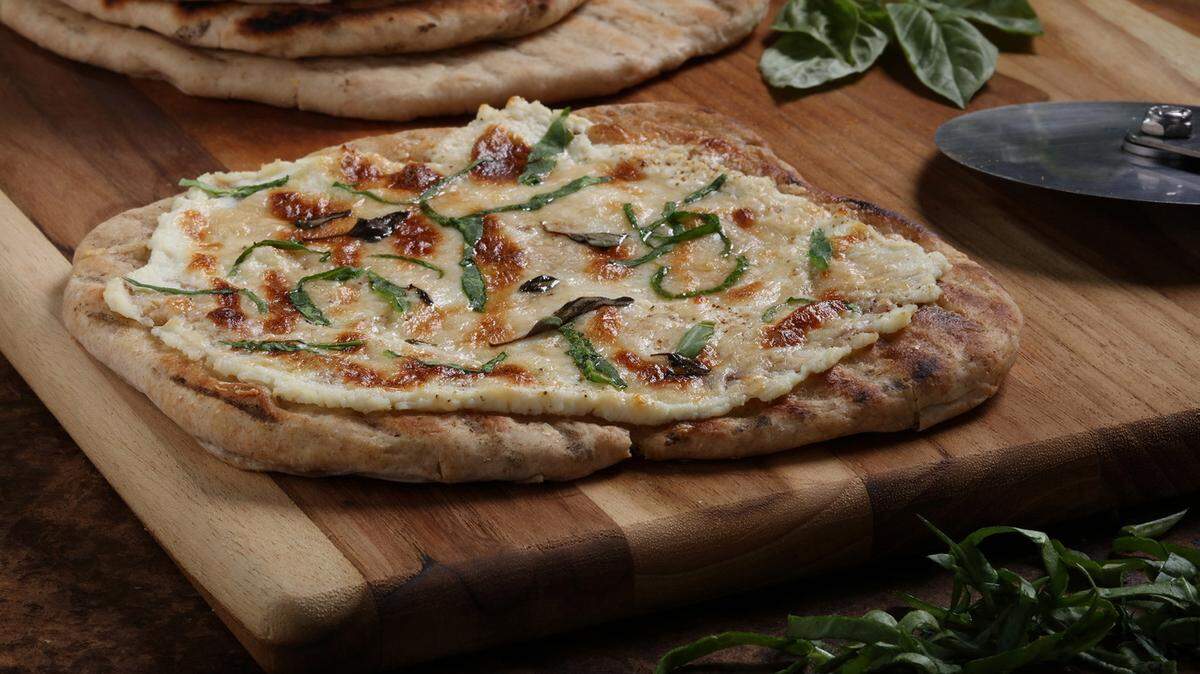 White pizza with basil has a ricotta cheese base, sprinkled with shredded Romano and a drizzle of mascarpone.