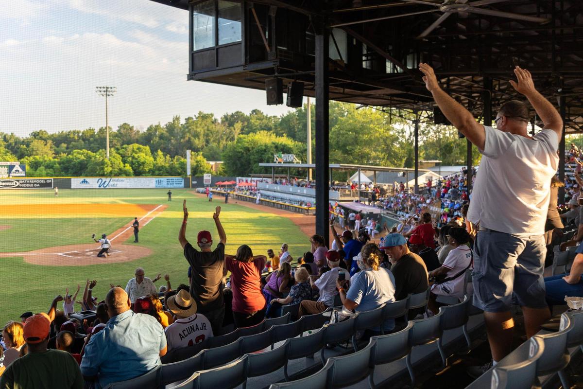Attendees stand up and wave their arms during a free t-shirt toss between innings during the Coastal Plains League All-Star Game on Monday, July 7, 2025, at Luther Williams Field in Macon, Georgia. The best players from across the summer collegiate baseball league, which includes the Macon Bacon, came to Macon for a two-day showcase.