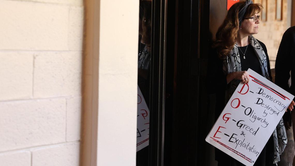 Laura Lucy, from Macon, Georgia, holds a sign criticizing the Department of Government Efficiency before the start of the town hall hosted by the local chapter of the American Federation of Government Employees (AFGE) on Thursday, March 20, 2025, at the Homer J. Walker Civic Center in Warner Robins, Georgia. Rep. Sanford Bishop (D-GA) spoke to constituents’ concerns about cutting federal programs and policies from President Donald Trump. AFGE also invited Rep. Austin Scott (R-GA), who did not attend.