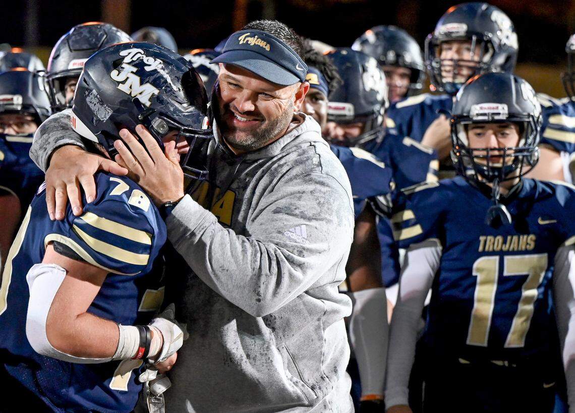 John Milledge head coach J.T. Wall hugs Hayden Hulett (78) while celebrating the Trojans’ 49-0 win over Deerfield-Windsor in the GIAA AAA Championship game.