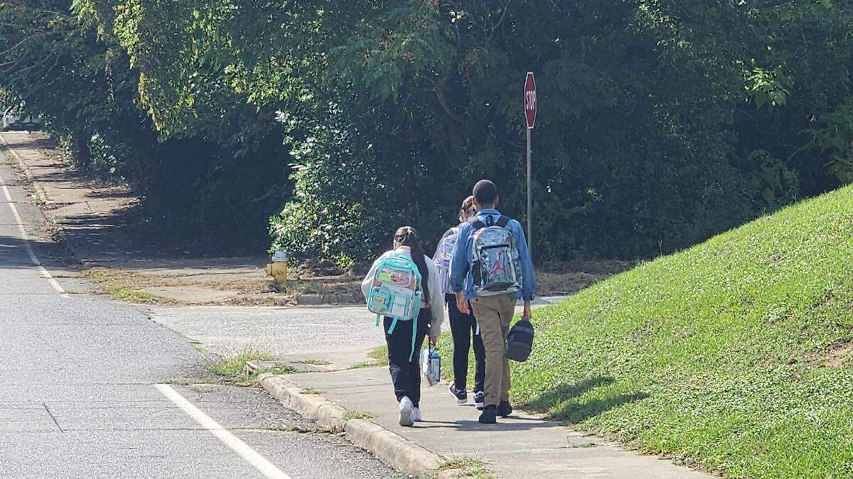 Burdell-Hunt Magnet Elementary School kids walk down a sidewalk in East Macon with overgrown foliage, raising neighborhood worries about pedestrian safety.