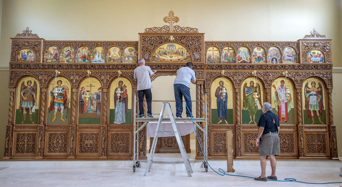 Iconographer Elias Dimakis, left, helps woodworker Thanos Athanasios install trim on June 29 on an icon screen Athanasios carved for Holy Cross Greek Orthodox Church. Athanasios and Dimakis traveled from Karditsa, Greece to install the screen and seventeen new icons Dimakis painted for the Church.