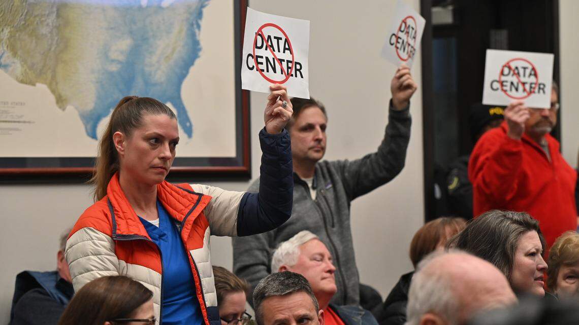Kristin Griffin, from Forsyth, Georgia, (left) holds up a “No Data Center” sign with other meeting attendees on Wednesday, Jan. 14, 2026, at Forsyth City Hall in Forsyth, Georgia. The commission split the vote 3-3 on approving a conditional rezoning proposal for a proposed data center in Forsyth.
