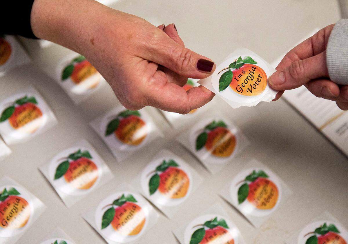 FILE - In this March 1, 2016 file photo, poll worker Delores Peterson, left, hands a sticker to a voter after they casted their ballot in Georgia’s primary election at a polling site in Atlanta. Georgians have a week left to vote early in primary runoff elections set for July 26. Secretary of State Brian Kemp’s office reports that more than 53,000 people cast ballots for races around the state since July 5. (AP Photo/David Goldman)