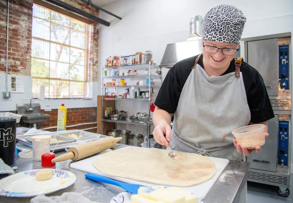 Saranne Ezelle sprinkles cinnamon sugar on dough while making cinnamon rolls at Old Mill Market Company located at 94 East Adams Street in Forsyth.