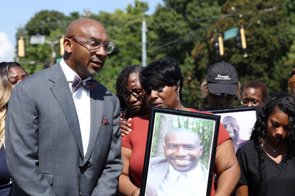 Attorney Mawuli Davis of Davis Bozeman Law stands with Paula Platt, mother of Stephen Fossett, who holds a picture of her son during a news conference discussing an investigation into Fossett’s death in 2024.