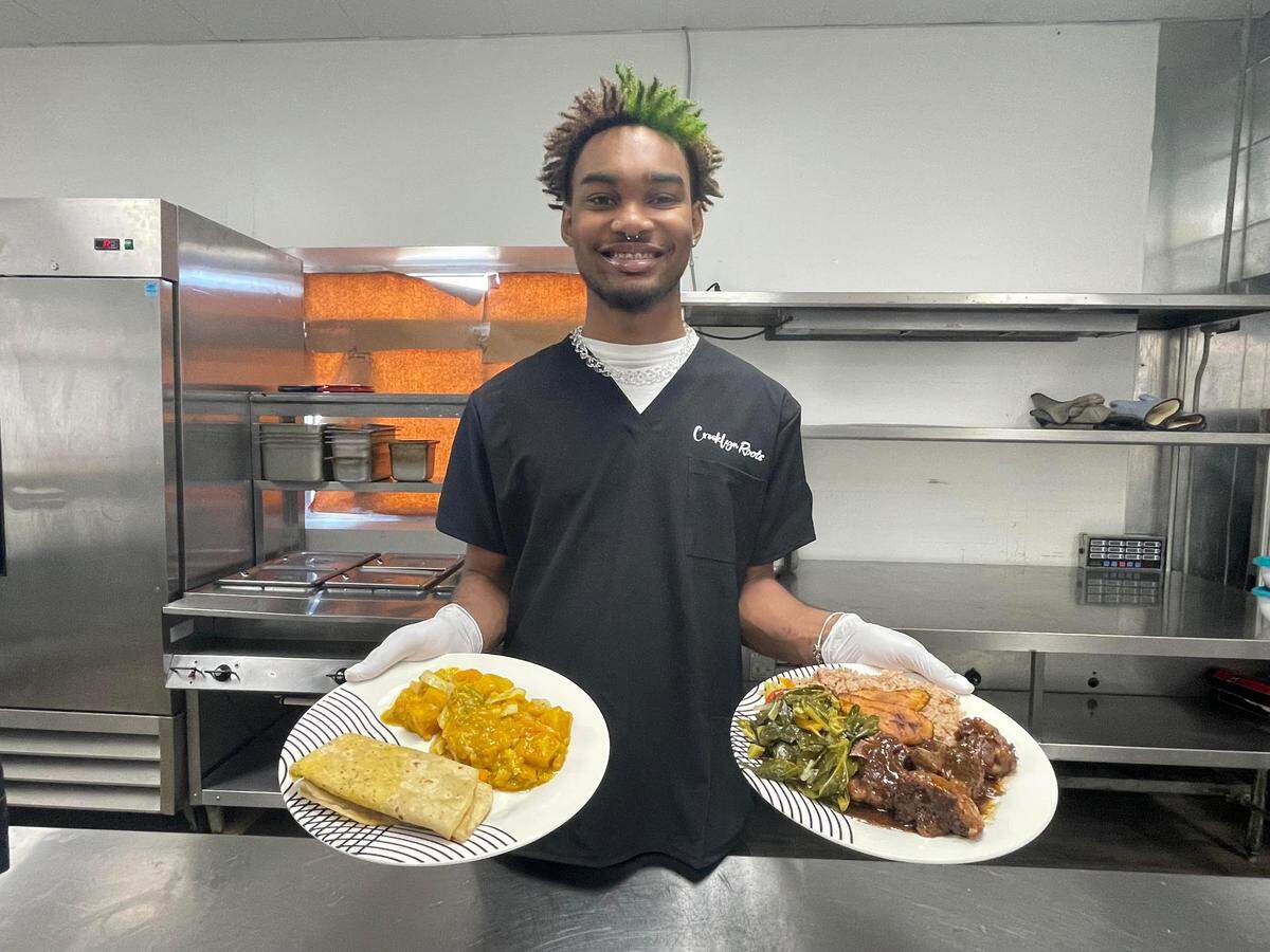 Tyler Cunningham, who works in the kitchen of his family’s new Byron restaurant, Crooklyn Roots, shows off two Jamaican dishes: vegan curry vegetables with roti skin and oxtails with brown rice and collard greens.