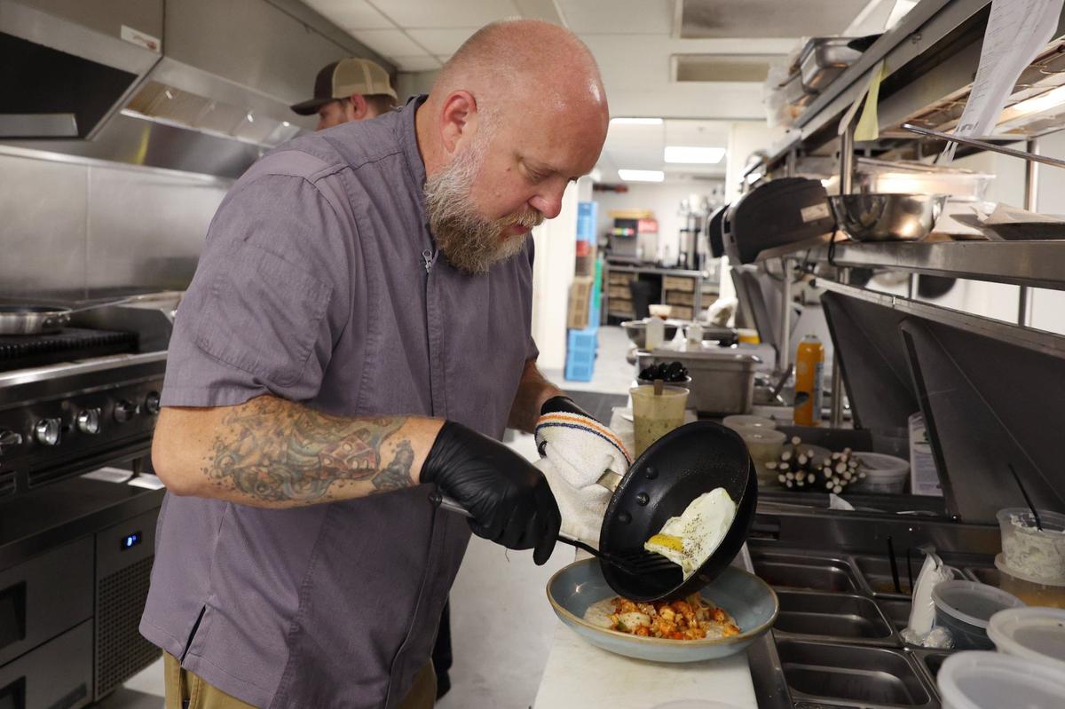 Hotel Forty Five executive chef Jayson Reynolds plates a sunny side up egg on top of shrimp and oyster grits in the kitchen of Loom on Tuesday, Aug. 6, 2024, in downtown Macon, Georgia. Tuesday marked only the second day of breakfast service at Loom, a new addition since Reynolds’ hiring. Reynolds said that he is still working to perfect the menu and establish an identity for Loom under his leadership.