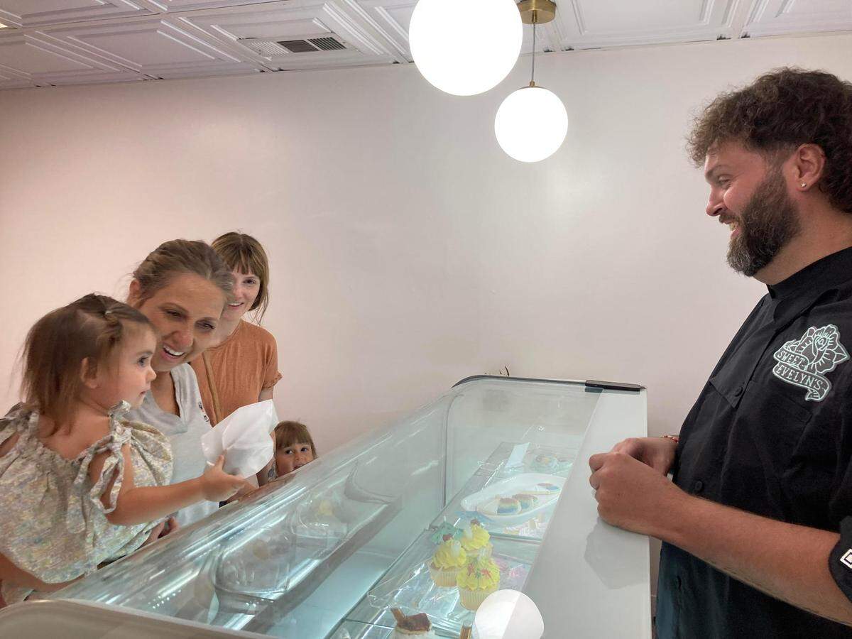 Quincy Benitez, in the arms of her grandmother, Lannette Tomlin, gets a cookie from Cory Jones, cookie artist and owner of Sweet Evelyn’s in downtown Perry while her mom, Tyger Benitez and sister, Clover, look on. Tomlin and her husband, Michael, own Clover Wine Merchant across the street.